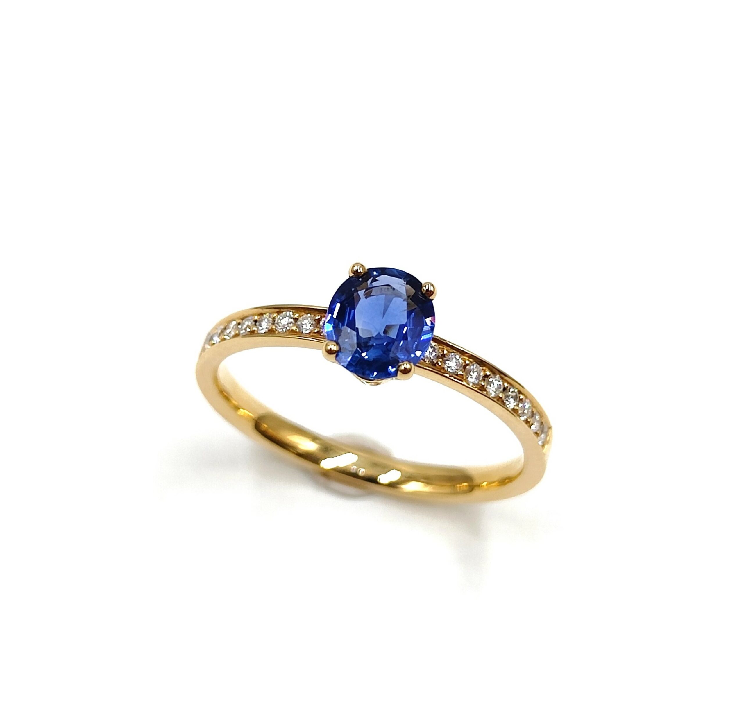 Bague en or jaune serti 4 griffes avec un saphir bleu rond proéminent, l'anneau est orné d'une rangée de petits diamants étincelants.